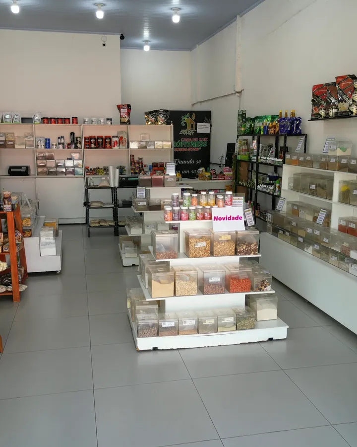 Interior da Casa de Raiz Prófitness: gôndola de granel com castanhas e amendoins, prateleiras de suplementos e parede de ervas